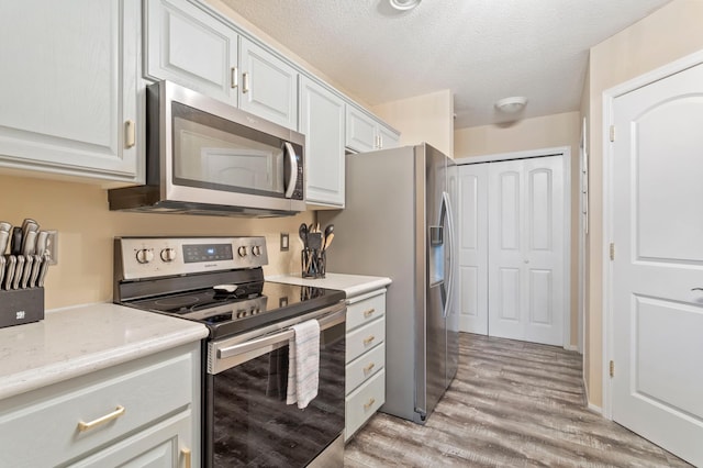8475 121st Ave N, Champlin, MN 55316 - kitchen featuring appliances with stainless steel finishes, light wood-style floors, white cabinetry, a textured ceiling, and light stone countertops