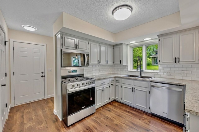 101 Sunset Dr S, Minnetonka, MN 55305 - kitchen with stainless steel appliances, a textured ceiling, backsplash, wood finished floors, and light stone countertops