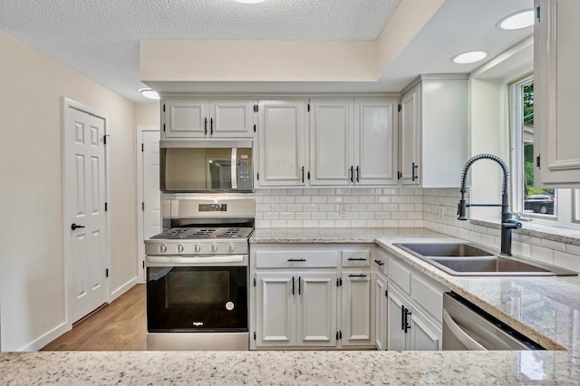 101 Sunset Dr S, Minnetonka, MN 55305 - kitchen featuring stainless steel appliances, tasteful backsplash, light stone countertops, light wood-type flooring, and a textured ceiling