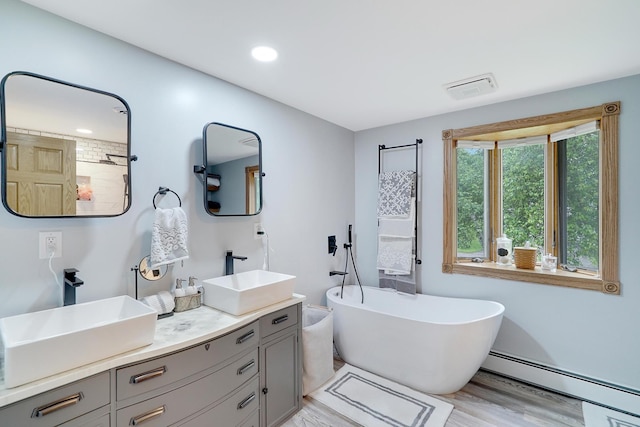 108 1st St, Kenyon, MN 55946 - full bath with a baseboard radiator, double vanity, a freestanding tub, wood finished floors, and recessed lighting