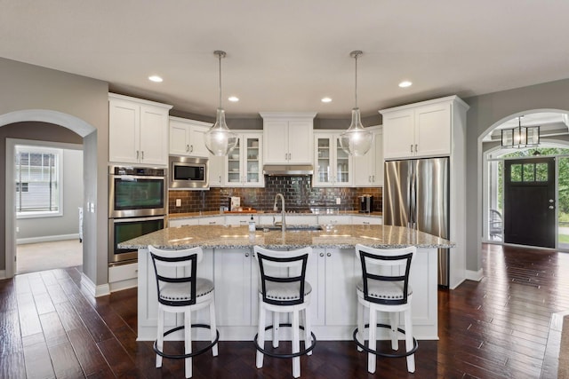 3365 Osgood Way N, Baytown Twp, MN 55082 - kitchen featuring stainless steel appliances, arched walkways, white cabinetry, a kitchen island with sink, and glass insert cabinets