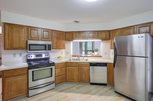 3801 98th St Unit 108, Bloomington, MN 55431 - kitchen with appliances with stainless steel finishes, light wood-type flooring, brown cabinetry, light countertops, and a textured ceiling