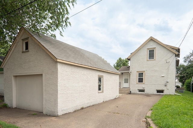 1303 Fremont Ave, Saint Paul, MN 55106 - view of property exterior featuring asphalt driveway, a garage, entry steps, roof with shingles, and stucco siding