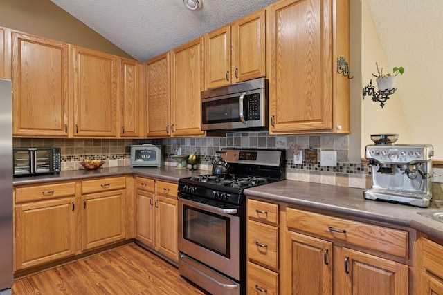8547 Grove Cir, Shakopee, MN 55379 - kitchen featuring appliances with stainless steel finishes, lofted ceiling, dark countertops, decorative backsplash, and a textured ceiling