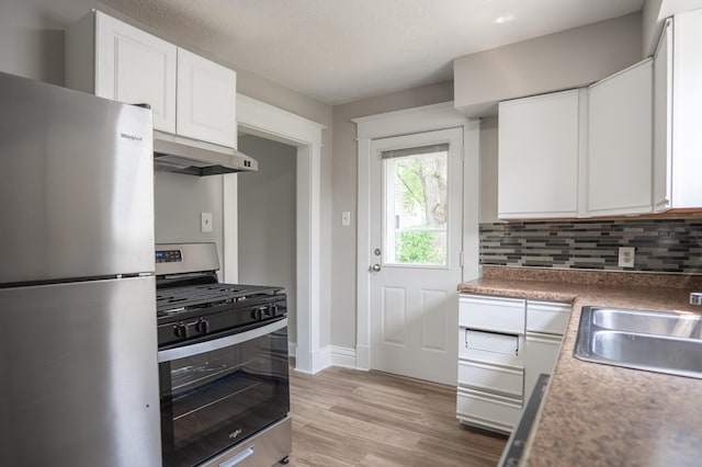 938 Cypress St, Saint Paul, MN 55106 - kitchen featuring appliances with stainless steel finishes, under cabinet range hood, decorative backsplash, white cabinetry, and light wood-style floors