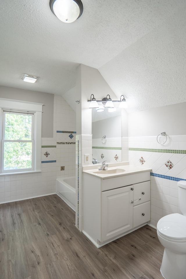 938 Cypress St, Saint Paul, MN 55106 - full bathroom featuring tile walls, a textured ceiling, wood finished floors, vanity, and lofted ceiling