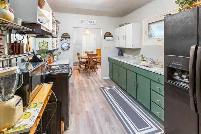 kitchen with black fridge, green cabinetry, light wood-style flooring, light countertops, and white cabinetry