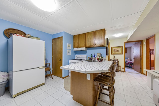 4820 Echo Ct, Faribault, MN 55021 - kitchen with white appliances, tile countertops, light tile patterned floors, a kitchen bar, and brown cabinetry