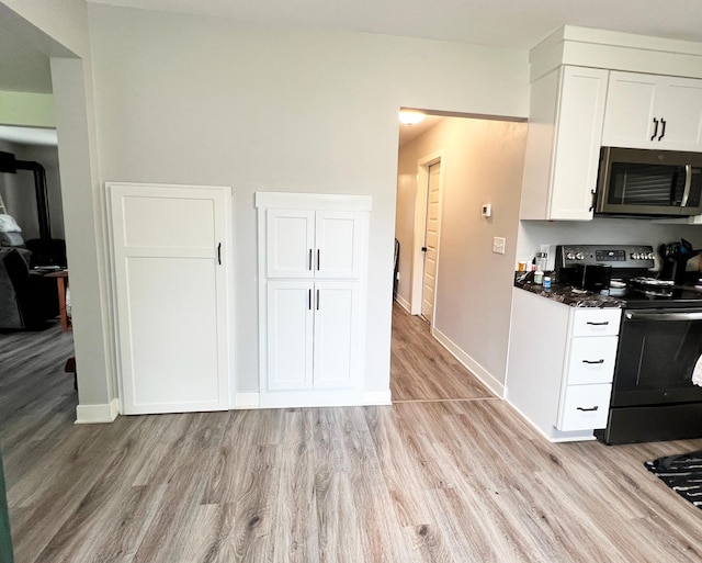 534 Main St, Perham, MN 56573 - kitchen featuring stainless steel microwave, black electric range, light wood-style flooring, white cabinetry, and dark stone counters