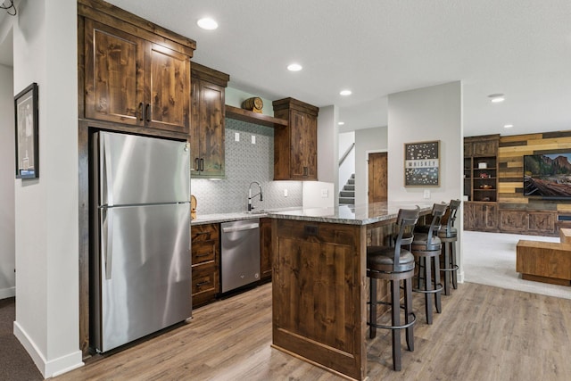 14217 Packard St NE, Ham Lake, MN 55304 - kitchen with stainless steel appliances, light wood-type flooring, stone counters, decorative backsplash, and a breakfast bar