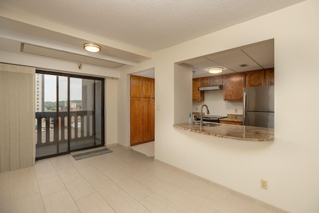 220 Broadway Ave S Unit 1221, Rochester, MN 55904 - kitchen with freestanding refrigerator, brown cabinets, under cabinet range hood, light stone countertops, and a textured ceiling