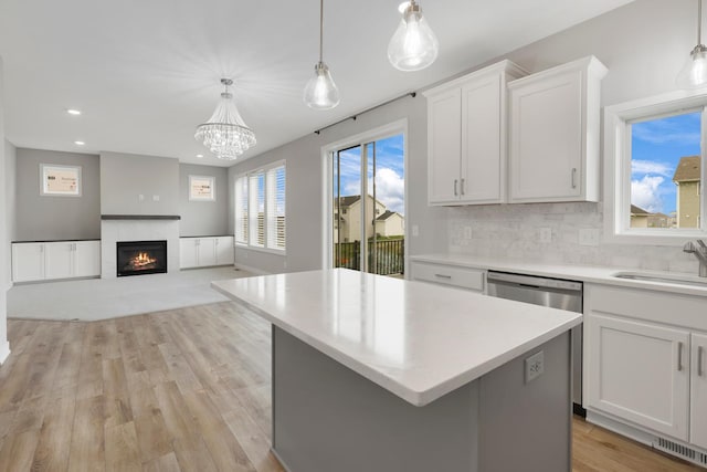 14320 Alder Way, Rosemount, MN 55068 - kitchen featuring light countertops, stainless steel dishwasher, a warm lit fireplace, white cabinetry, and a center island