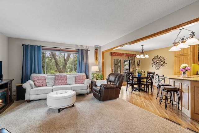 13048 Jay St NW, Coon Rapids, MN 55448 - living room with healthy amount of natural light, a chandelier, light wood-style floors, a textured ceiling, and a glass covered fireplace