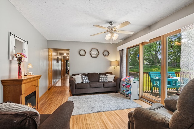 2796 269th Ave NE, Isanti, MN 55040 - living room featuring ceiling fan, light wood finished floors, a textured ceiling, and a warm lit fireplace