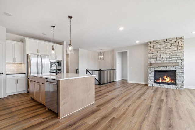 10180 Shadyview Ln N, Maple Grove, MN 55311 - kitchen featuring stainless steel appliances, light wood finished floors, white cabinetry, tasteful backsplash, and a center island with sink
