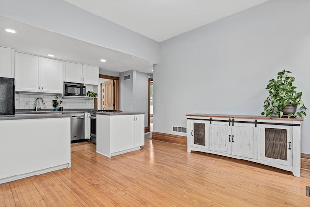 1813 11th Ave S, Minneapolis, MN 55404 - kitchen featuring black microwave, dishwasher, dark countertops, white cabinets, and light wood-style flooring