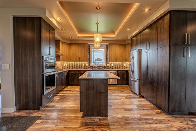 3405 4th St E, West Fargo, ND 58078 - kitchen featuring appliances with stainless steel finishes, a kitchen island, tasteful backsplash, a raised ceiling, and wood finished floors
