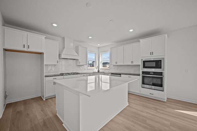 11532 Polaris Ln N, Dayton, MN 55369 - kitchen featuring stainless steel appliances, premium range hood, a kitchen island, light wood finished floors, and white cabinets