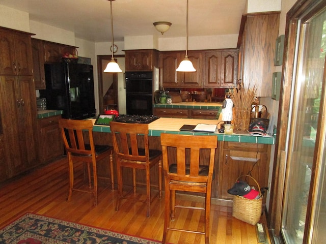 4523 Waville Rd NE, Bemidji, MN 56601 - kitchen featuring black appliances, tile countertops, light wood-type flooring, a peninsula, and hanging light fixtures