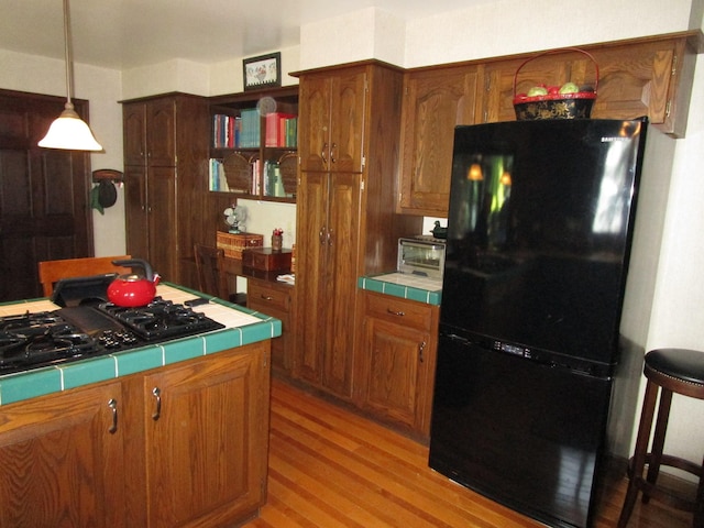 4523 Waville Rd NE, Bemidji, MN 56601 - kitchen with black appliances, tile counters, light wood-style floors, hanging light fixtures, and brown cabinetry