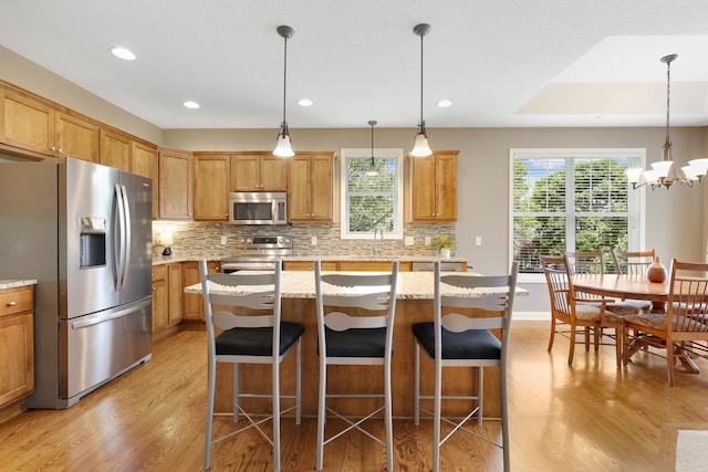 kitchen featuring appliances with stainless steel finishes, light wood finished floors, backsplash, recessed lighting, and a center island