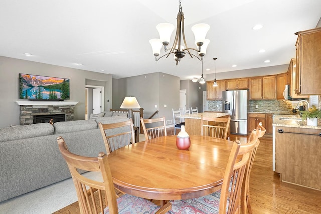 dining space with light wood-type flooring, a chandelier, recessed lighting, and a stone fireplace