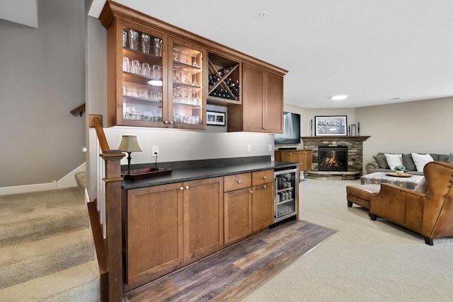 indoor wet bar with dark colored carpet, beverage cooler, stairway, and a fireplace