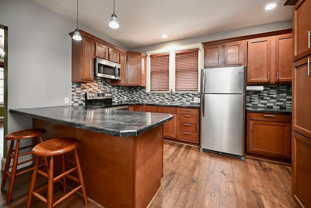 579 4th St, Winona, MN 55987 - kitchen featuring appliances with stainless steel finishes, a peninsula, dark countertops, brown cabinets, and a kitchen bar