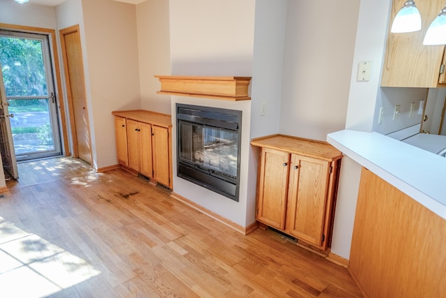 1865 Donegal Dr Unit 3, Woodbury, MN 55125 - kitchen featuring light wood-style flooring, a glass covered fireplace, light countertops, and decorative light fixtures