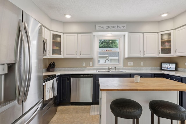 1475 Eldridge Ave E, Maplewood, MN 55109 - kitchen featuring appliances with stainless steel finishes, wood counters, a breakfast bar, a textured ceiling, and white cabinets