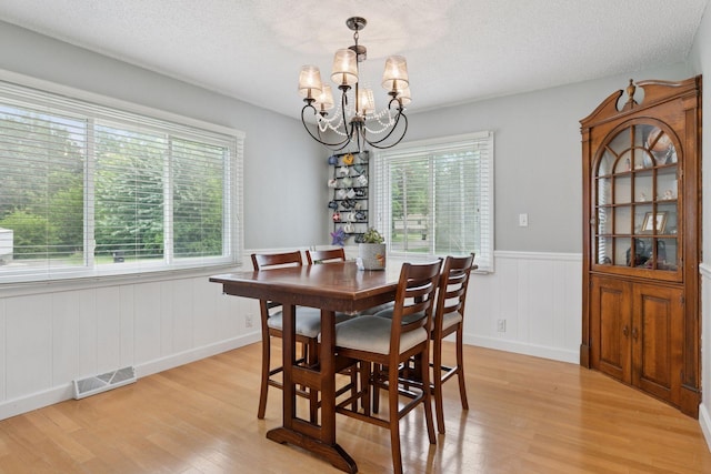 1475 Eldridge Ave E, Maplewood, MN 55109 - dining area with a chandelier, light wood-type flooring, a wainscoted wall, and a textured ceiling