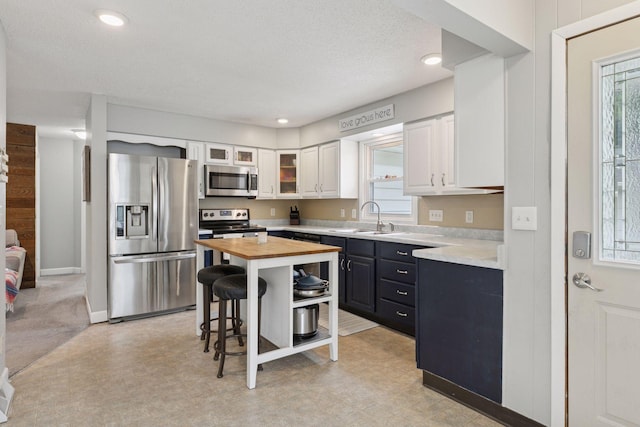 1475 Eldridge Ave E, Maplewood, MN 55109 - kitchen featuring appliances with stainless steel finishes, wooden counters, white cabinetry, glass insert cabinets, and light floors