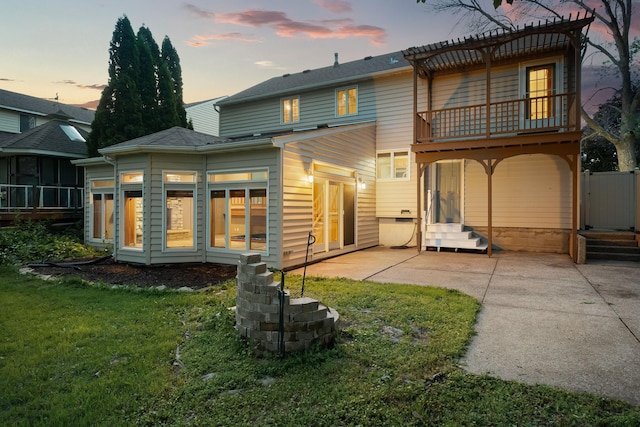 1218 4th Ave SE, Austin, MN 55912 - back of house at dusk featuring a balcony, a patio area, entry steps, and a yard