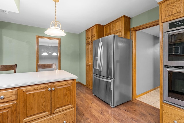 1218 4th Ave SE, Austin, MN 55912 - kitchen featuring appliances with stainless steel finishes, brown cabinetry, light wood finished floors, light countertops, and hanging light fixtures