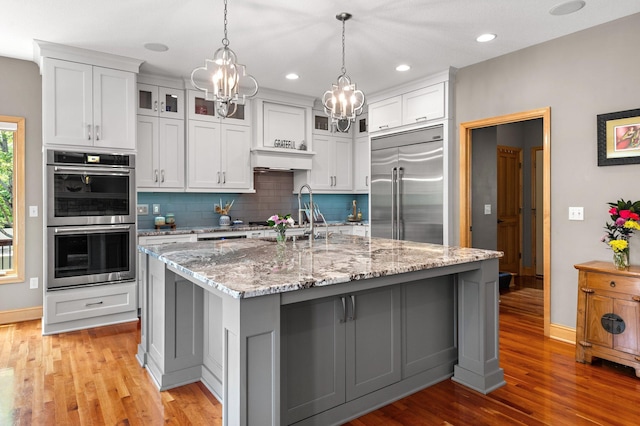 2334 Veterans Memorial Blvd NW, Andover, MN 55304 - kitchen with appliances with stainless steel finishes, a chandelier, backsplash, light wood-style flooring, and glass insert cabinets