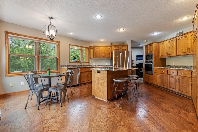 18505 210th Ave NE, Paynesville, MN 56362 - kitchen featuring stainless steel appliances, a center island, brown cabinetry, a breakfast bar area, and dark wood finished floors