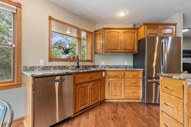 18505 210th Ave NE, Paynesville, MN 56362 - kitchen featuring appliances with stainless steel finishes, stone counters, dark wood-type flooring, brown cabinets, and a textured ceiling