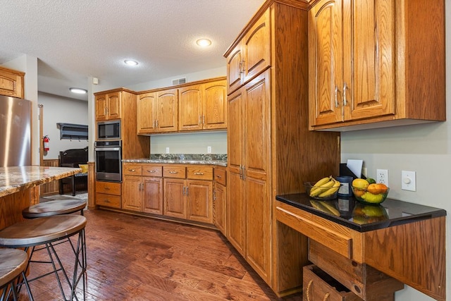 18505 210th Ave NE, Paynesville, MN 56362 - kitchen with stainless steel appliances, brown cabinetry, dark wood-style floors, a textured ceiling, and recessed lighting
