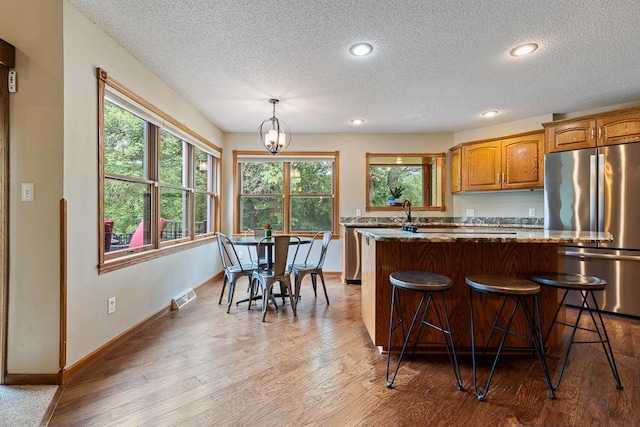 18505 210th Ave NE, Paynesville, MN 56362 - kitchen featuring freestanding refrigerator, a textured ceiling, a kitchen island, a kitchen breakfast bar, and wood finished floors