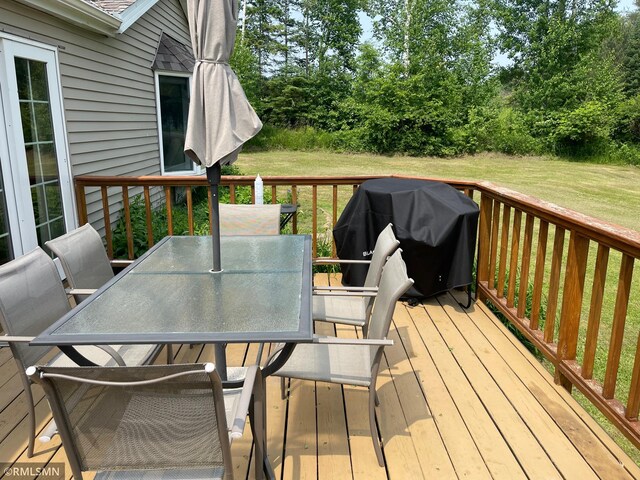 21507 County Road 560, Goodland Twp, MN 55742 - wooden deck with grilling area, outdoor dining area, a lawn, and view of scattered trees