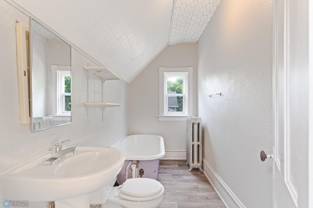 824 9th St N, Fargo, ND 58102 - bathroom with radiator, wood finished floors, a soaking tub, vaulted ceiling, and a textured wall