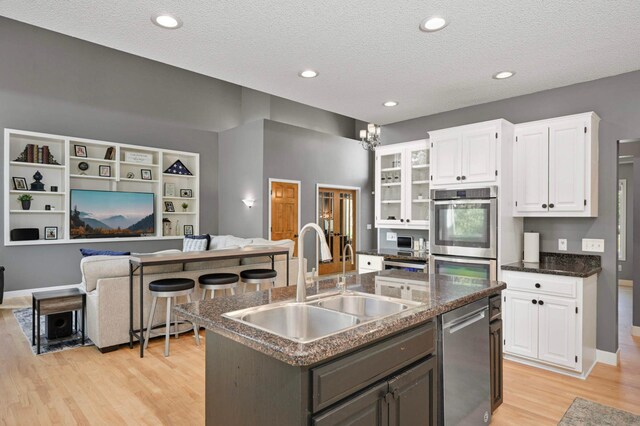 3583 Woodland Trl, Eagan, MN 55123 - kitchen featuring appliances with stainless steel finishes, white cabinetry, light wood-style flooring, open floor plan, and a center island with sink