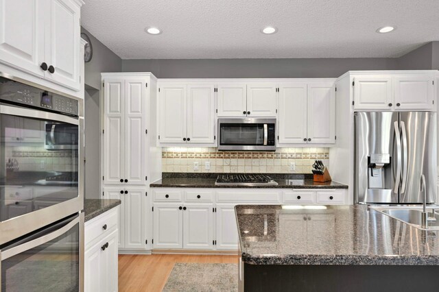 3583 Woodland Trl, Eagan, MN 55123 - kitchen featuring appliances with stainless steel finishes, white cabinets, light wood-style floors, dark stone counters, and tasteful backsplash