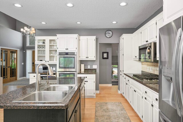 3583 Woodland Trl, Eagan, MN 55123 - kitchen featuring appliances with stainless steel finishes, a kitchen island with sink, light wood finished floors, white cabinetry, and a textured ceiling