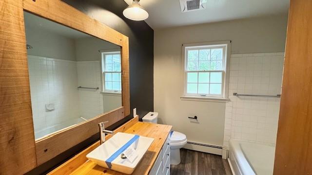 811 Myrtle St, Buffalo, MN 55313 - full bathroom featuring baseboard heating, vanity, wood finished floors, and shower / washtub combination