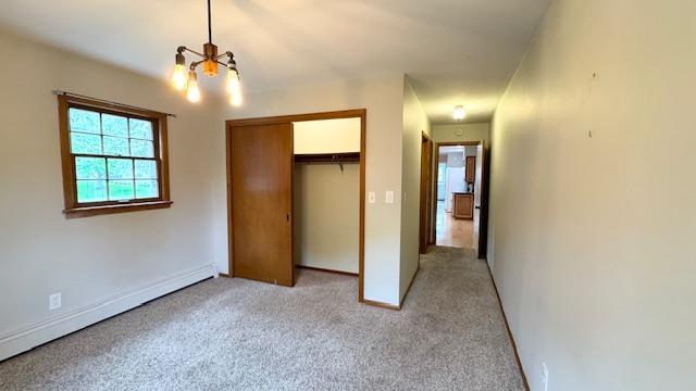 811 Myrtle St, Buffalo, MN 55313 - unfurnished bedroom with a chandelier, a baseboard heating unit, light colored carpet, and a closet