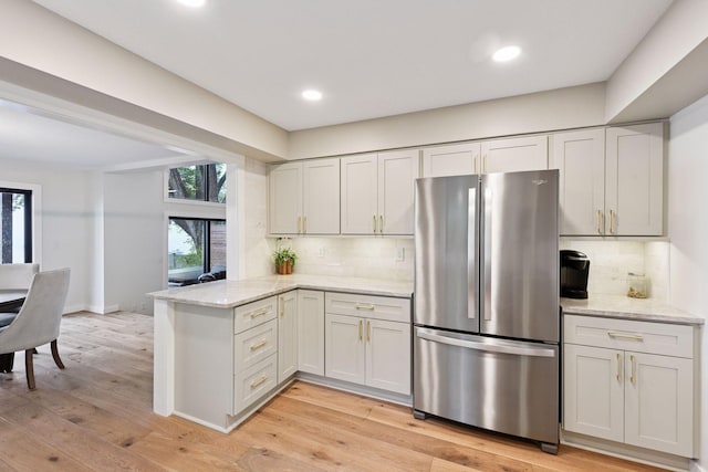 6641 Halstead Ave, Mound, MN 55364 - kitchen with freestanding refrigerator, a peninsula, decorative backsplash, light stone counters, and light wood-style flooring