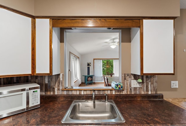 1202 Matteson St, Faribault, MN 55021 - kitchen featuring white microwave, a wood stove, a ceiling fan, vaulted ceiling, and dark countertops