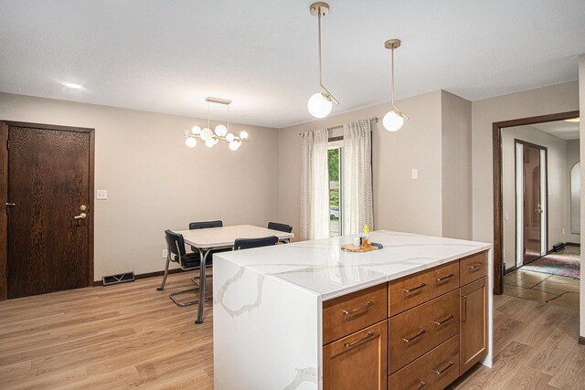 201 Elm St, Luverne, MN 56156 - kitchen with light wood finished floors, decorative light fixtures, brown cabinets, light stone countertops, and a kitchen island