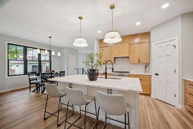 3909 54th St, Edina, MN 55424 - kitchen featuring decorative backsplash, light wood-type flooring, a kitchen island with sink, light stone counters, and a kitchen breakfast bar